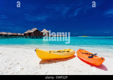 Giallo e orangel Canoe sulla spiaggia tropicale con vilas in background Foto Stock