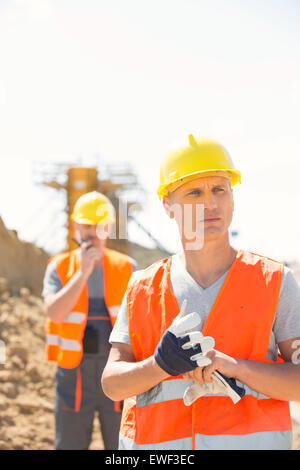 Lavoratore di sesso maschile permanente al sito di costruzione con il collega in background Foto Stock