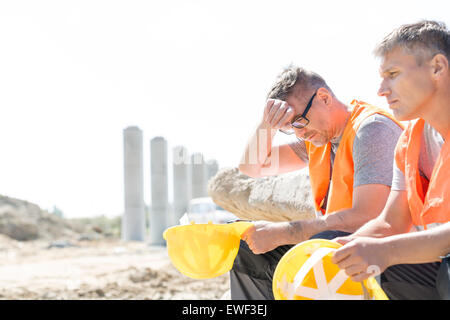 Stanco di supervisor seduta con un collega sul sito in costruzione Foto Stock