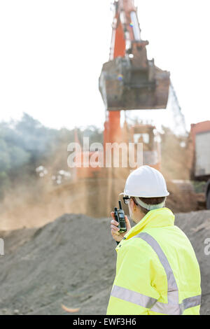 Vista laterale dell'ingegnere utilizzando un walkie-talkie al sito in costruzione Foto Stock