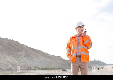 Fiducioso supervisore maschio utilizzando un walkie-talkie sul sito di costruzione contro il cielo chiaro Foto Stock