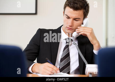 Imprenditore conversando su telefono fisso mentre la scrittura su carta Foto Stock