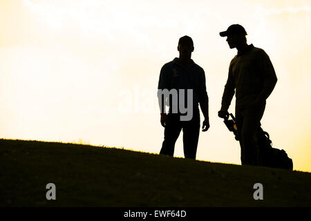 Silhouette di giovani uomini in piedi in campo da golf con trolley Foto Stock