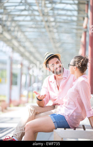 Felice l'uomo a parlare con una donna durante la seduta sul banco sotto ombra Foto Stock