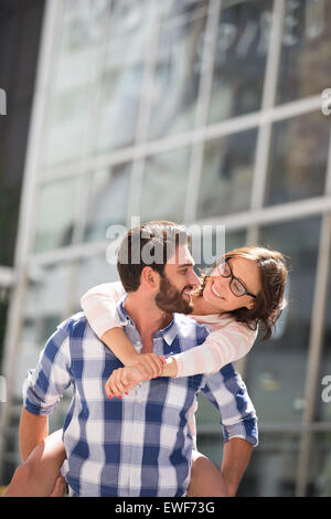 Coppia felice guardando ogni altro mentre godendo piggyback Ride in città Foto Stock