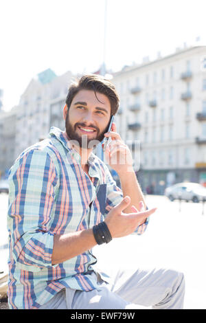 Uomo sorridente che guarda lontano mentre si usa il cellulare in città Foto Stock