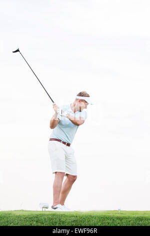 Lunghezza intera della metà di uomo adulto swinging golf club contro il cielo chiaro Foto Stock
