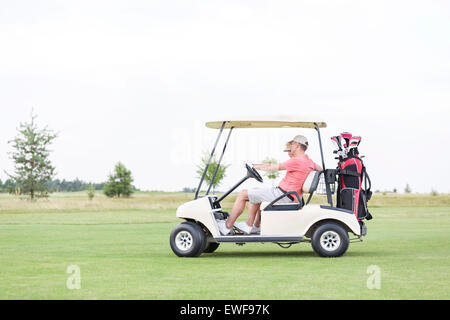 Vista laterale del giovane seduto in golf cart contro il cielo chiaro Foto Stock