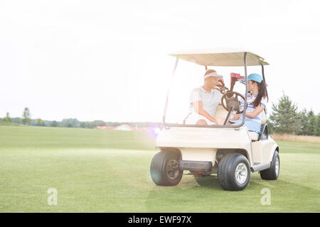 Giovane guardando ogni altro mentre è seduto in golf cart contro il cielo chiaro Foto Stock