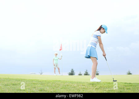 Donna che gioca a golf con femmina amico contro sky Foto Stock