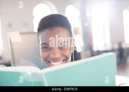 Ritratto imprenditrice sorridente dietro il libro in ufficio Foto Stock