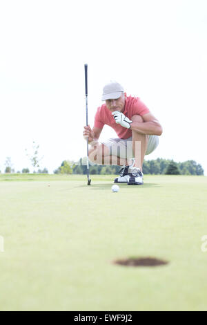 Uomo di mezza età guardando a sfera mentre accovacciato sul campo da golf Foto Stock