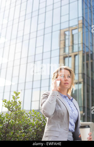 Imprenditrice utilizzando il telefono cellulare al di fuori di edificio per uffici Foto Stock
