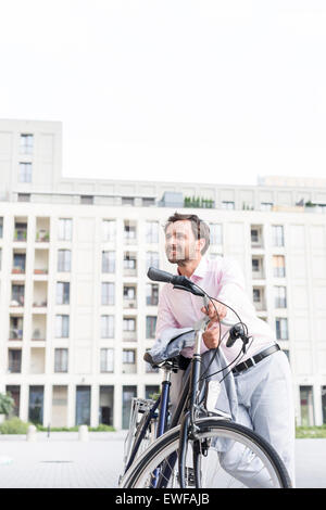 Imprenditore pensosa appoggiata sulla bicicletta all'aperto Foto Stock