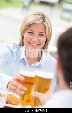 Bella imprenditrice tostare il bicchiere da birra con il collega di sesso maschile al ristorante Foto Stock