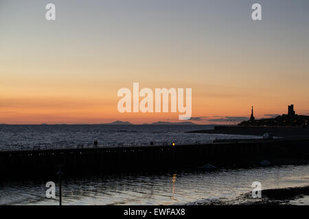 Aberystwyth al tramonto, con il memoriale di guerra e il castello di sillhouette e Snowdonia montagne in distanza. Foto Stock