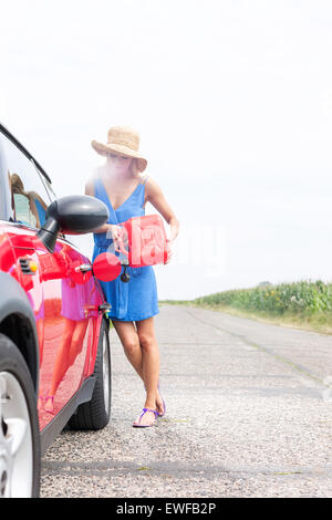 Lunghezza intera della donna il rifornimento auto sulla strada di campagna contro il cielo chiaro Foto Stock