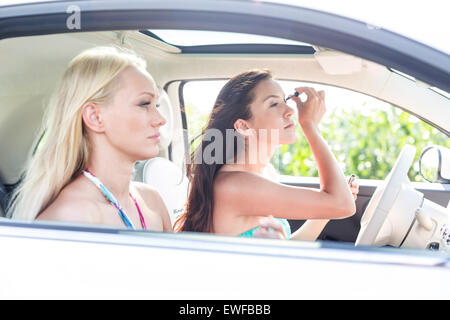 Donna facendo il make-up con femmina amico seduti in auto Foto Stock