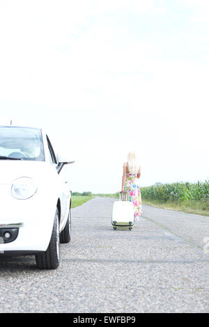 Vista posteriore della donna con bagagli lasciando ripartiti in auto sulla strada di campagna Foto Stock