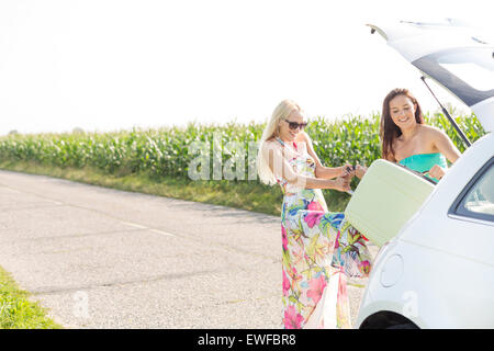 Felici donne carico dei bagagli nel baule auto contro il cielo chiaro Foto Stock