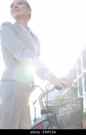 Basso angolo vista di imprenditrice in piedi con la bicicletta sulla giornata di sole Foto Stock