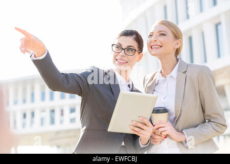 Felice imprenditrice che mostra qualcosa a un collega mentre si utilizza un tablet PC Foto Stock