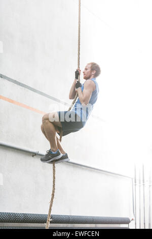 Vista laterale del determinato uomo corda di arrampicata in palestra crossfit Foto Stock