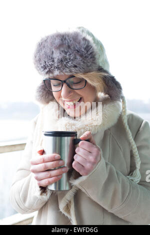 Allegra donna in abiti caldi tenendo isolato di contenitore per bevande Foto Stock