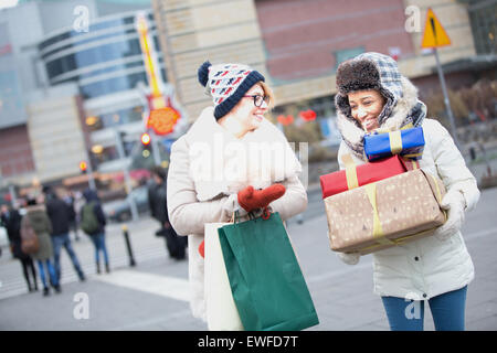 Felici donne con doni e borse per lo shopping a piedi su via della città durante il periodo invernale Foto Stock