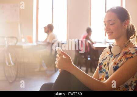 Sorridente casual imprenditrice sms sul cellulare in ufficio Foto Stock