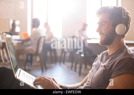 Imprenditore Casual indossando le cuffie e lavorare al computer portatile in ufficio Foto Stock