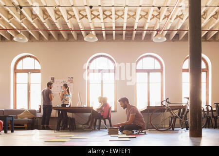 Imprenditore creativo su skateboard lavora al computer portatile sul pavimento in open office Foto Stock