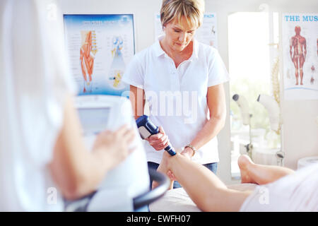 Terapista fisico usando la sonda ecografica sulla donna è la gamba Foto Stock