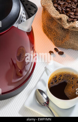 Una tazza calda di caffè nero con una riflessione sul lato di un bollitore elettrico Foto Stock