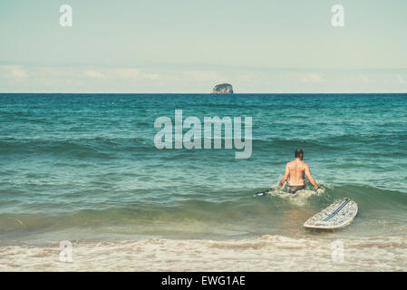 Un surfista maschile cavalca un'onda nell'oceano, bilanciandosi sulla sua tavola da surf. L'immagine cattura l'energia dell'oceano e l'abilità del surfista mentre naviga sull'onda. Foto Stock