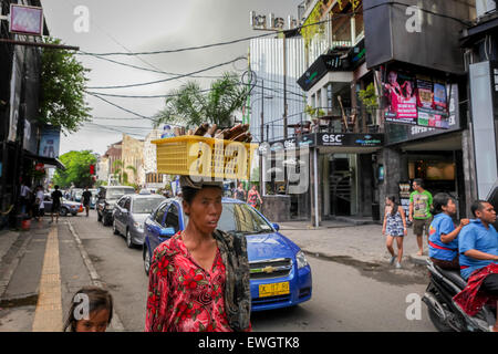 Donna balinese che trasporta oggetti d'artigianato e bottiglia d'acqua in testa a Legian Street, Bali. Foto Stock