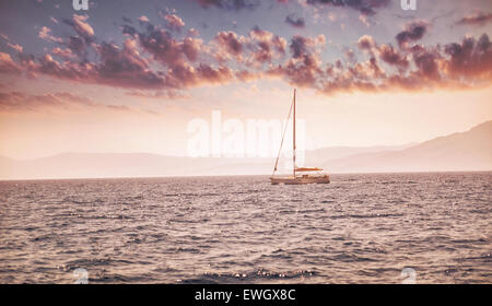 Paesaggio marino, barca a vela vela in la distanza in blanda rosa la luce del tramonto, vacanze romantiche in mare Foto Stock