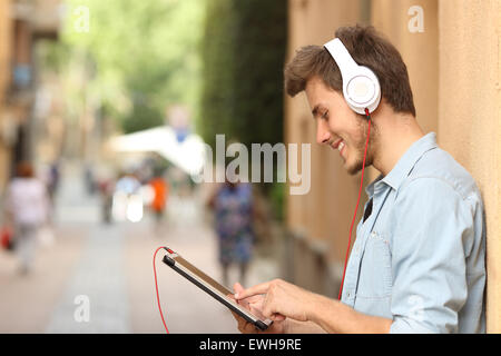 Profilo di un uomo con una tavoletta con le cuffie sulla strada e toccando lo schermo con il dito Foto Stock
