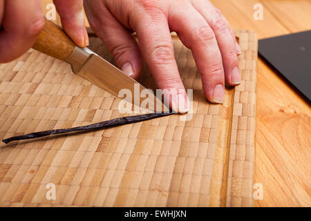Il taglio di aprire il baccello di vaniglia con un coltello sul bambù tagliere Foto Stock