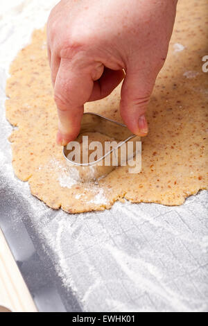 Tagliare fuori i biscotti a forma di cuore con cookie cutter da freschi di pasta biscotto Foto Stock