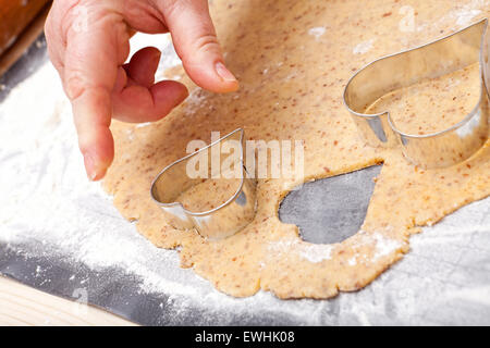 Tagliare fuori i biscotti a forma di cuore con cookie cutter da freschi di pasta biscotto Foto Stock