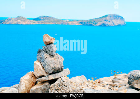 Primo piano di una pila di pietre equilibrato in Isola di Ibiza in Spagna, con il mar Mediterraneo e l'isola di Tagomago in backg Foto Stock