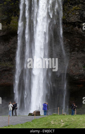 I turisti pongono per le fotografie di fronte a cascata Seljalandsfoss in Islanda Foto Stock