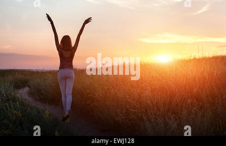 Libera felice giovane donna i bracci di sollevamento al tramonto nel campo d'estate. Sfondo Foto Stock