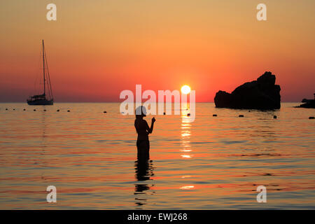 Una bella ragazza che fuma una sigaretta mentre si gode il tramonto Sopra la Baia di Ghajn Tuffieha a Malta Foto Stock