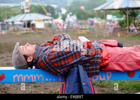 Festival di Glastonbury, Somerset, Regno Unito. Il 27 giugno 2015. Come il festival di Glastonbury si prepara per un altro giorno il sole torna e inizia ad asciugare il fango un festival goer dorme su un banco di lavoro. Credito: Tom Corban/Alamy Live News Foto Stock