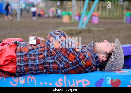 Festival di Glastonbury, Somerset, Regno Unito. Il 27 giugno 2015. Come il festival di Glastonbury si prepara per un altro giorno il sole torna e inizia ad asciugare il fango un festival goer dorme su un banco di lavoro. Credito: Tom Corban/Alamy Live News Foto Stock