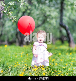 Funny bambina gioca con un palloncino rosso in un giardino Foto Stock