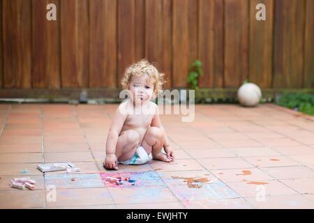 Divertente piccola bambina indossa un pannolino con pittura a Chalk nel cortile di una casa Foto Stock