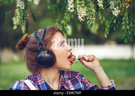 Ritratto di piuttosto attraente ragazza hipster cuffie. Ragazza leccare un lecca-lecca. Tonificazione caldo. Il concetto di vita felice. Foto Stock